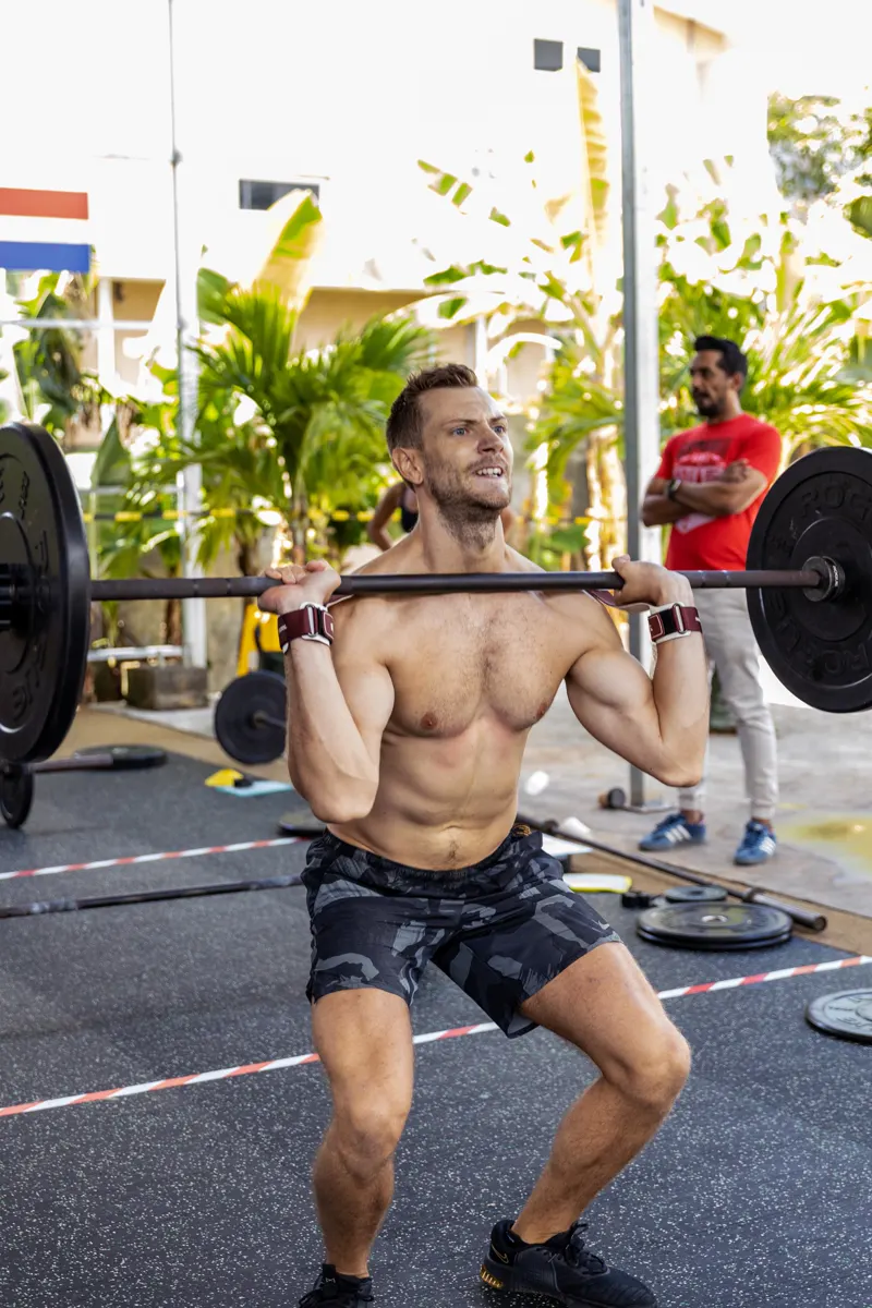 Un athlète descend en front squat, barre chargée posée sur les épaules, marquage au sol de la zone de compétition sous ses pieds.